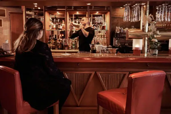 A man in a black dress sits at a bar with a woman in a black dress.