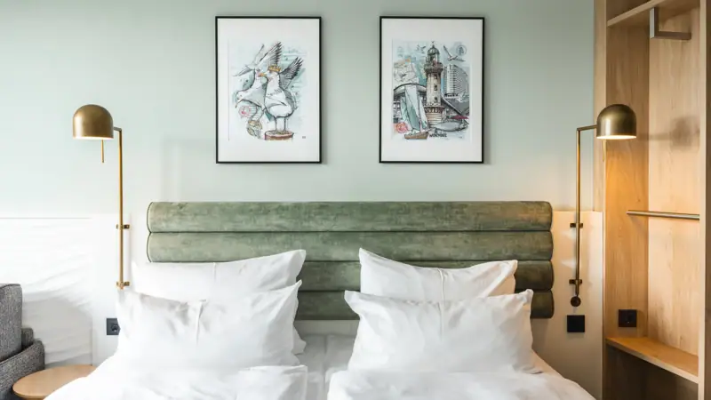 A bed with white cushions and a green headboard, flanked by two lamps.