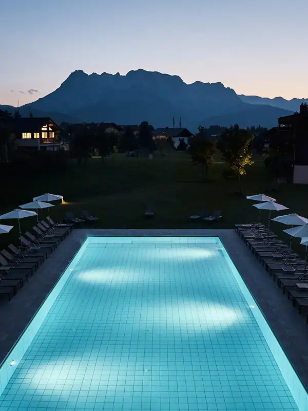 A pool with chairs and parasols in front of a house.
