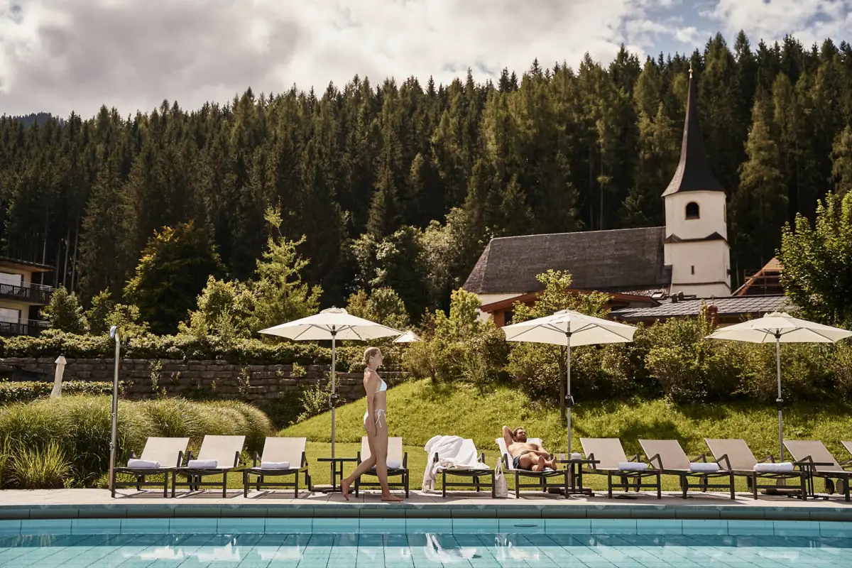 A woman walks along a pool where there are sunbeds.