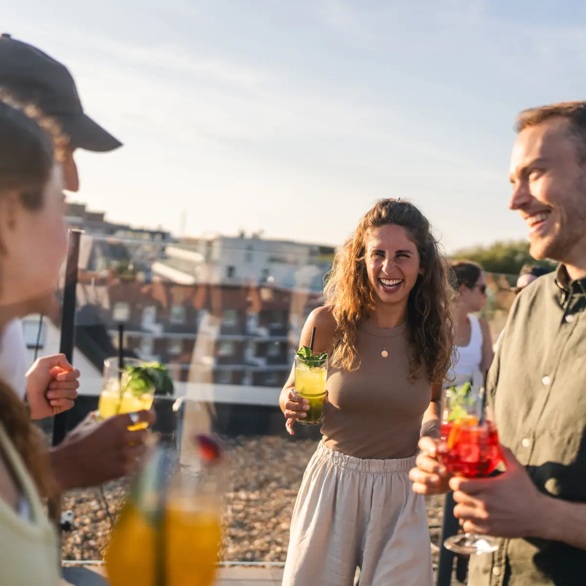 Group of celebrating people standing with cocktails on a roof terrace