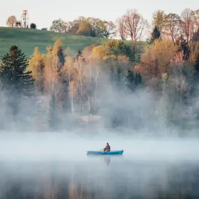 A person in a boat on a foggy lake.
