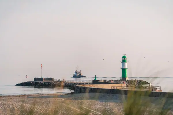 Warnemünde Strand Leuchtturm am Strand bei klarem Himmel und Wasser im Hintergrund.