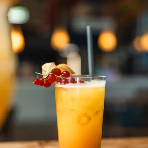 Drinks at aja Warnemünde A glass with an orange drink, straw and berries.