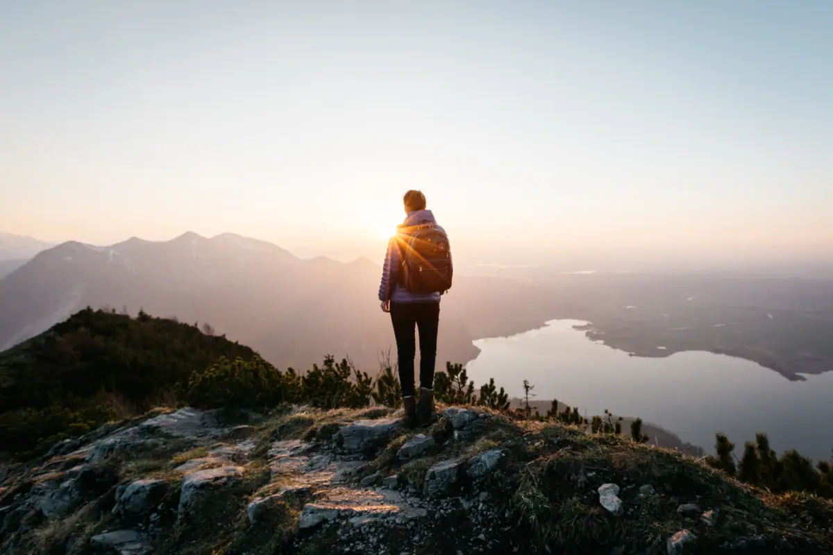 A person stands on a hill and looks into the sun.