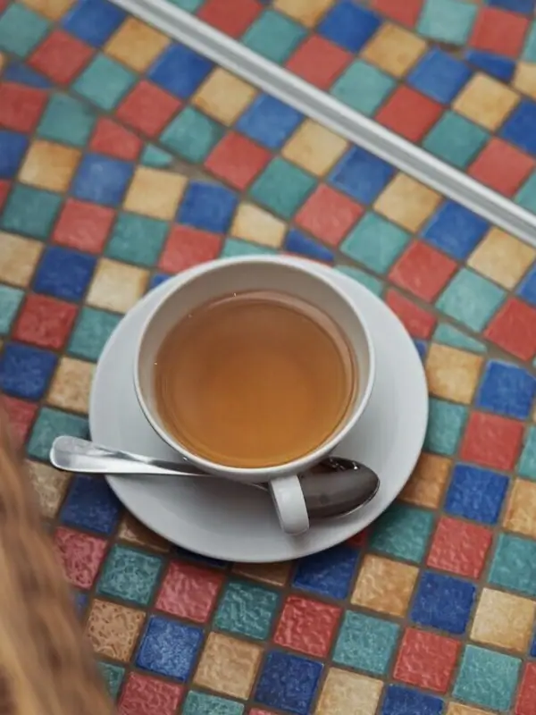 A cup of tea on a saucer on a colourful tiled floor.