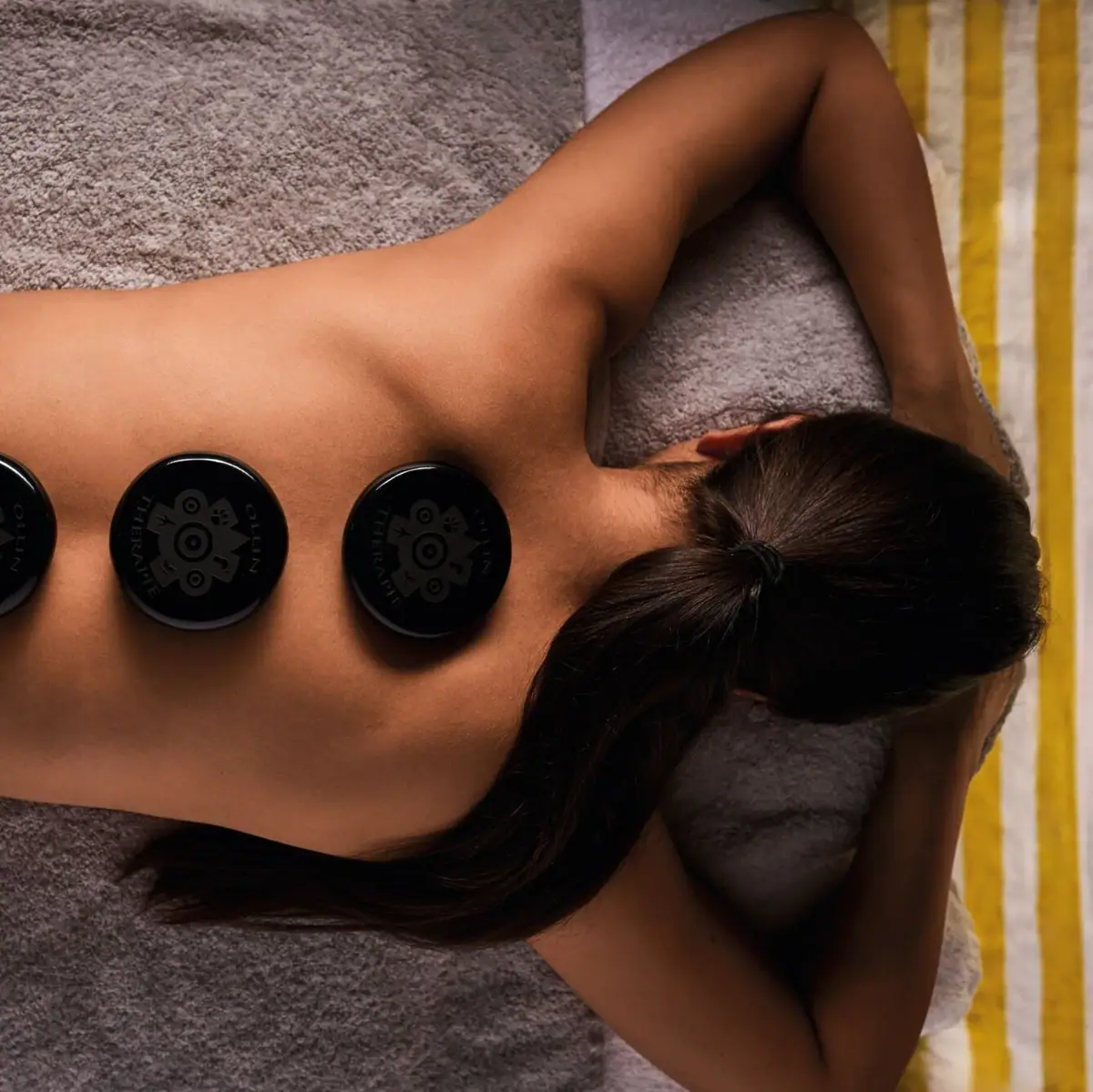 Hot stone massage A woman lies on a bed with several black stones on her back.