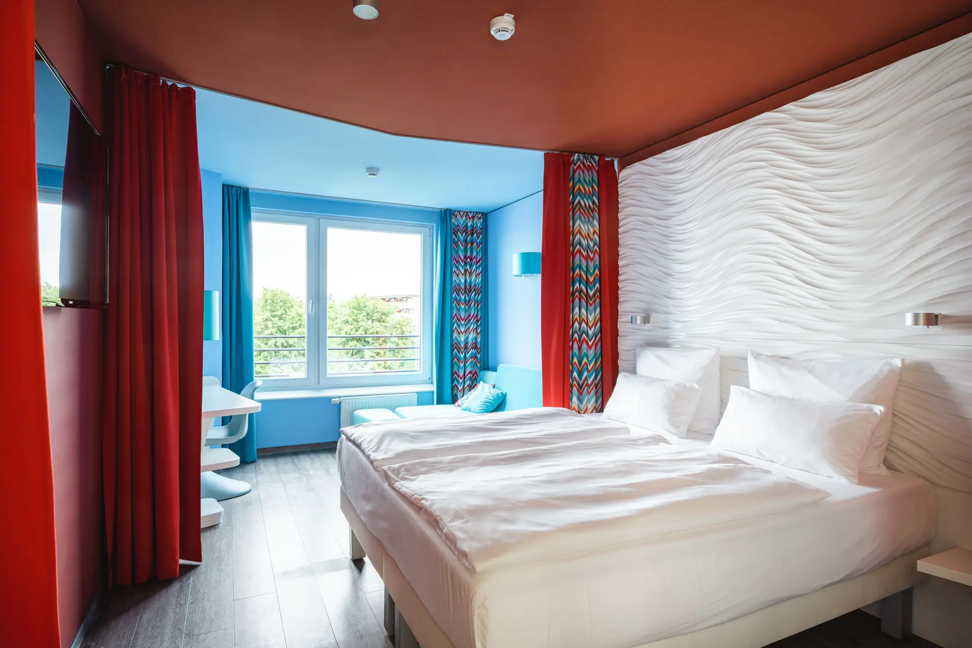 A room with two beds and red curtains in front of a window in the background