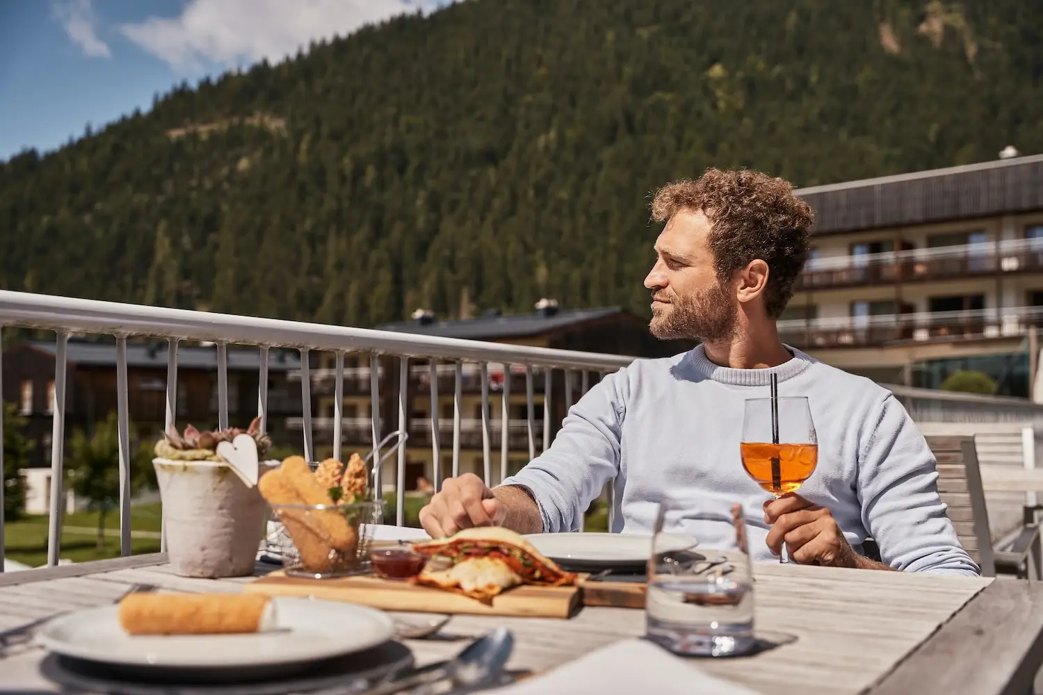 Man sitting at an outdoor table, surrounded by food and drink.