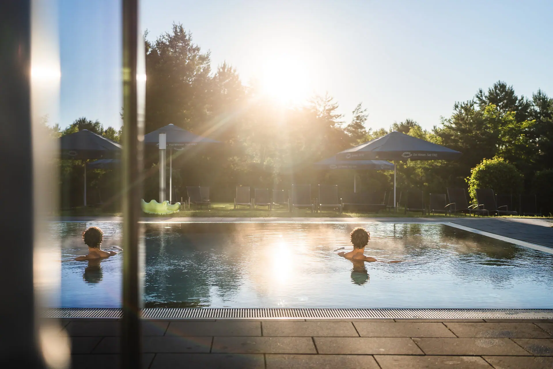 Ein Mensch schwimmt in einem Außenpool bei Sonnenschein.