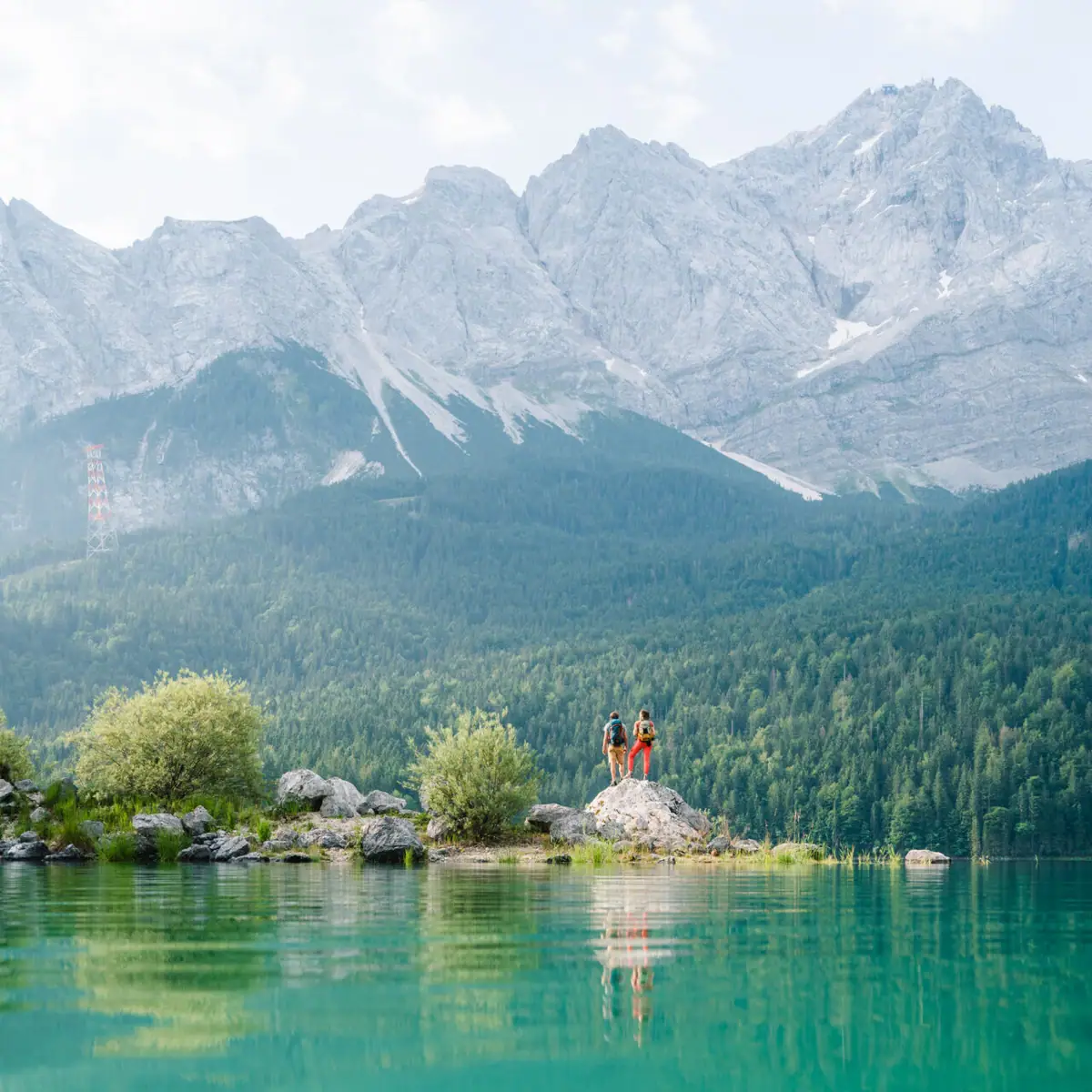 Eibsee Two people are standing on a rock in front of a body of water.
