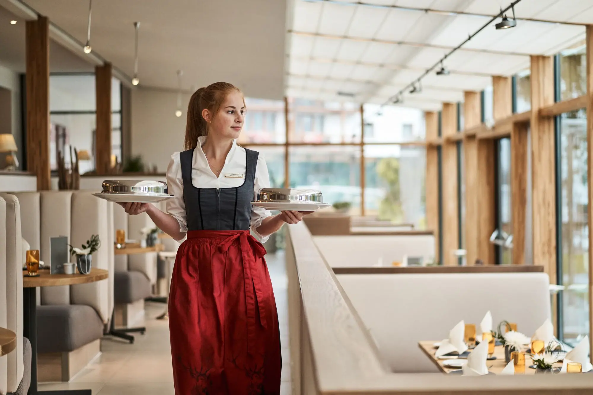 Waitress in a dirndl holds two plates as she walks through the restaurant.