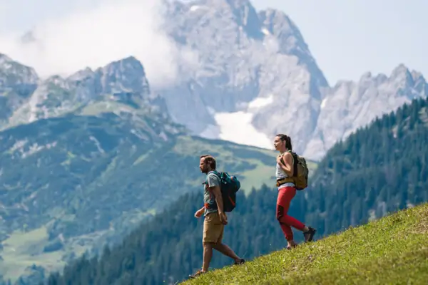 Two people hiking on a hill with mountains in the background.