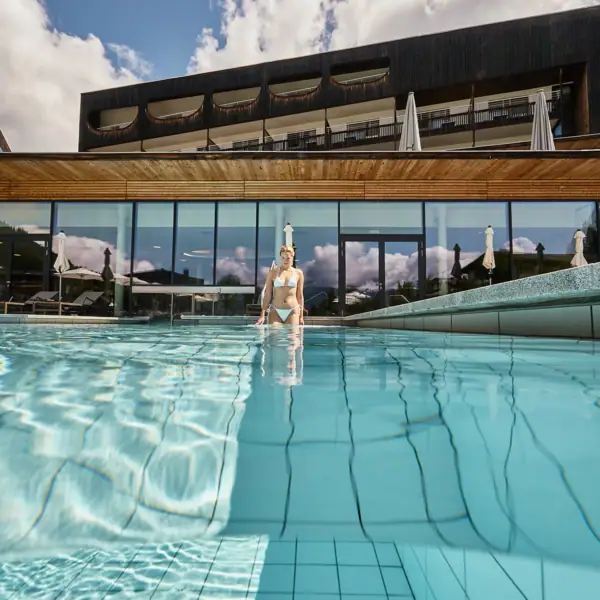 A woman in a swimming pool with the hotel in the background.