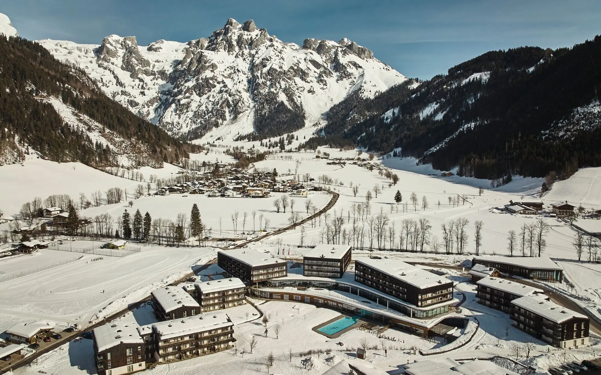 Group of buildings in a snowy valley with a mountain backdrop.