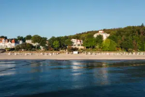 Ein strand vom Wasser aus fotografiert mit Bäumen und weißen Gebäuden.