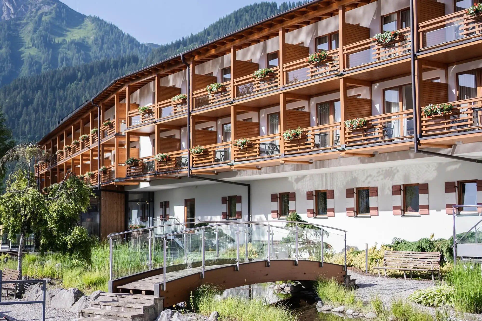 aja Bergresort Werfenweng with bridge and river, surrounded by mountains and trees.