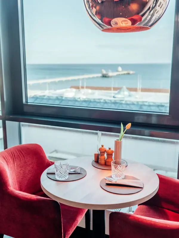 View from the JEDERMANNS restaurant in Grömitz A table with red chairs and a red lamp.