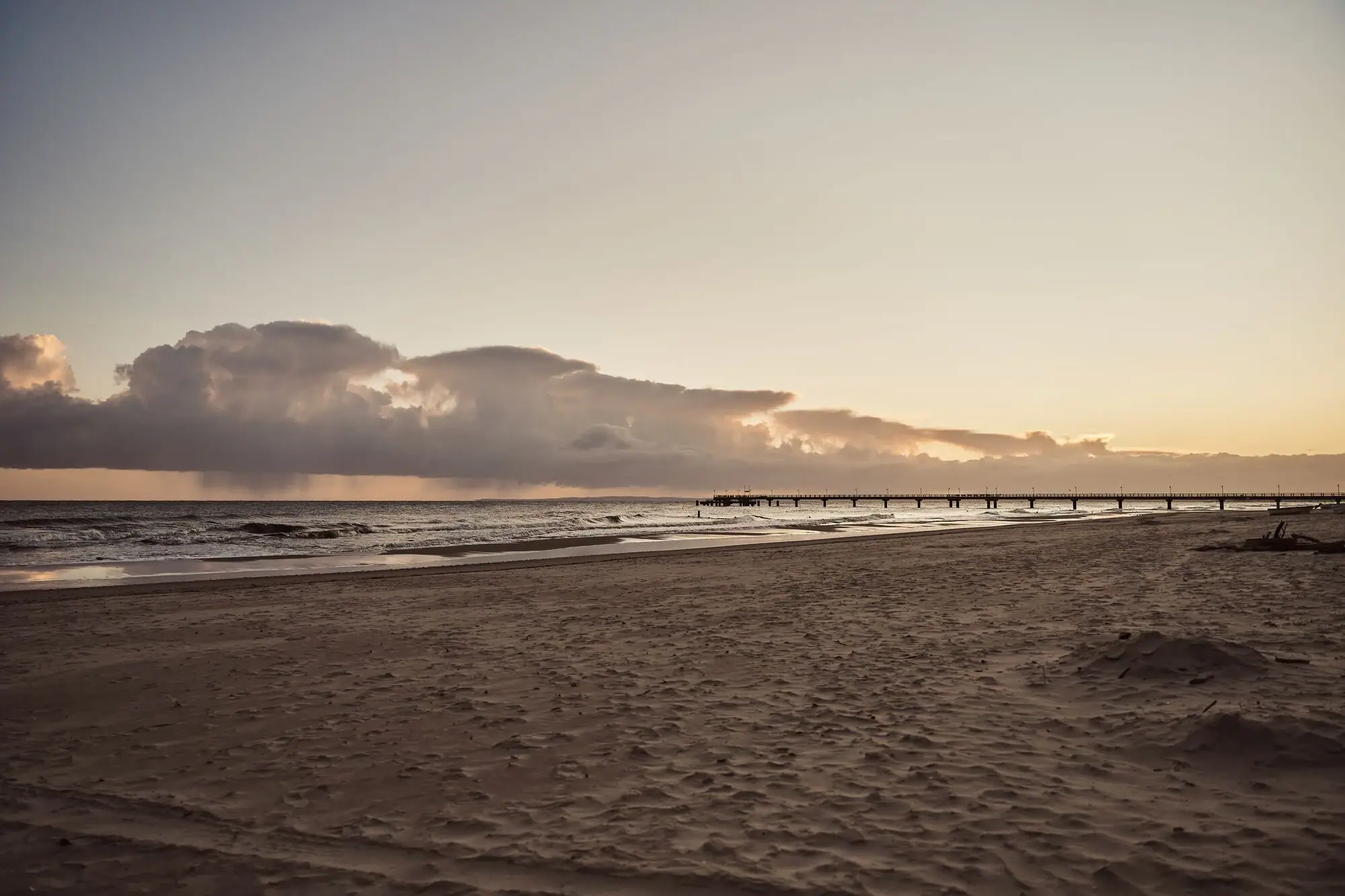 A beach with a pier and water in the foreground.