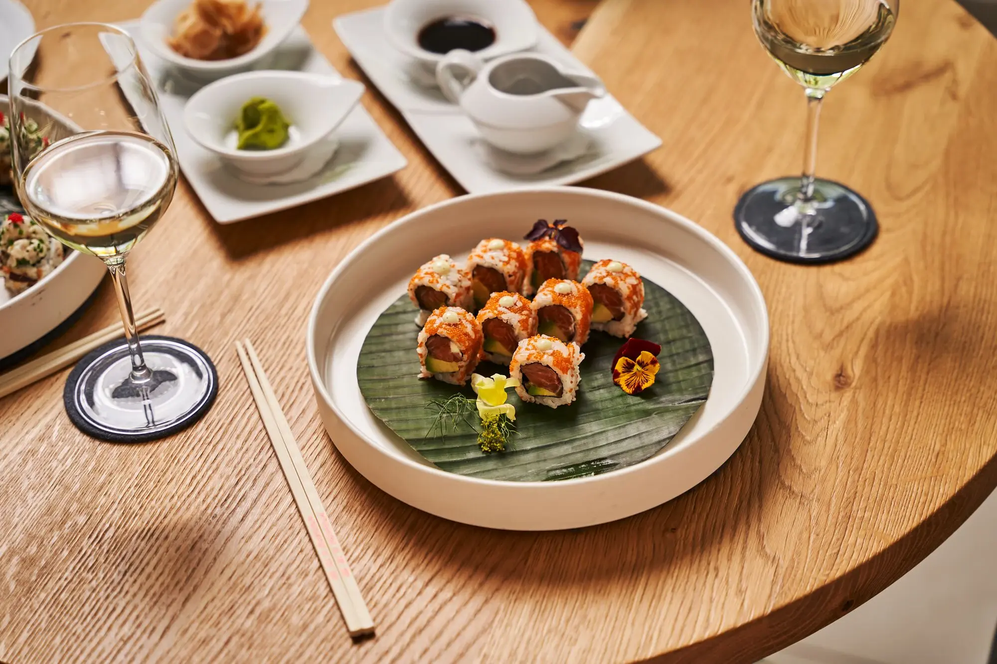 A plate of sushi next to glasses of wine on a table.