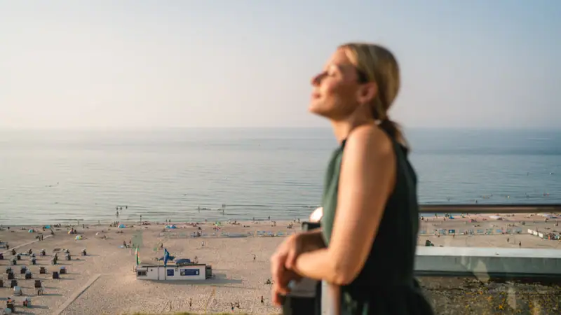 Rooms at the aja Warnemünde A woman stands on a railing overlooking a beach.