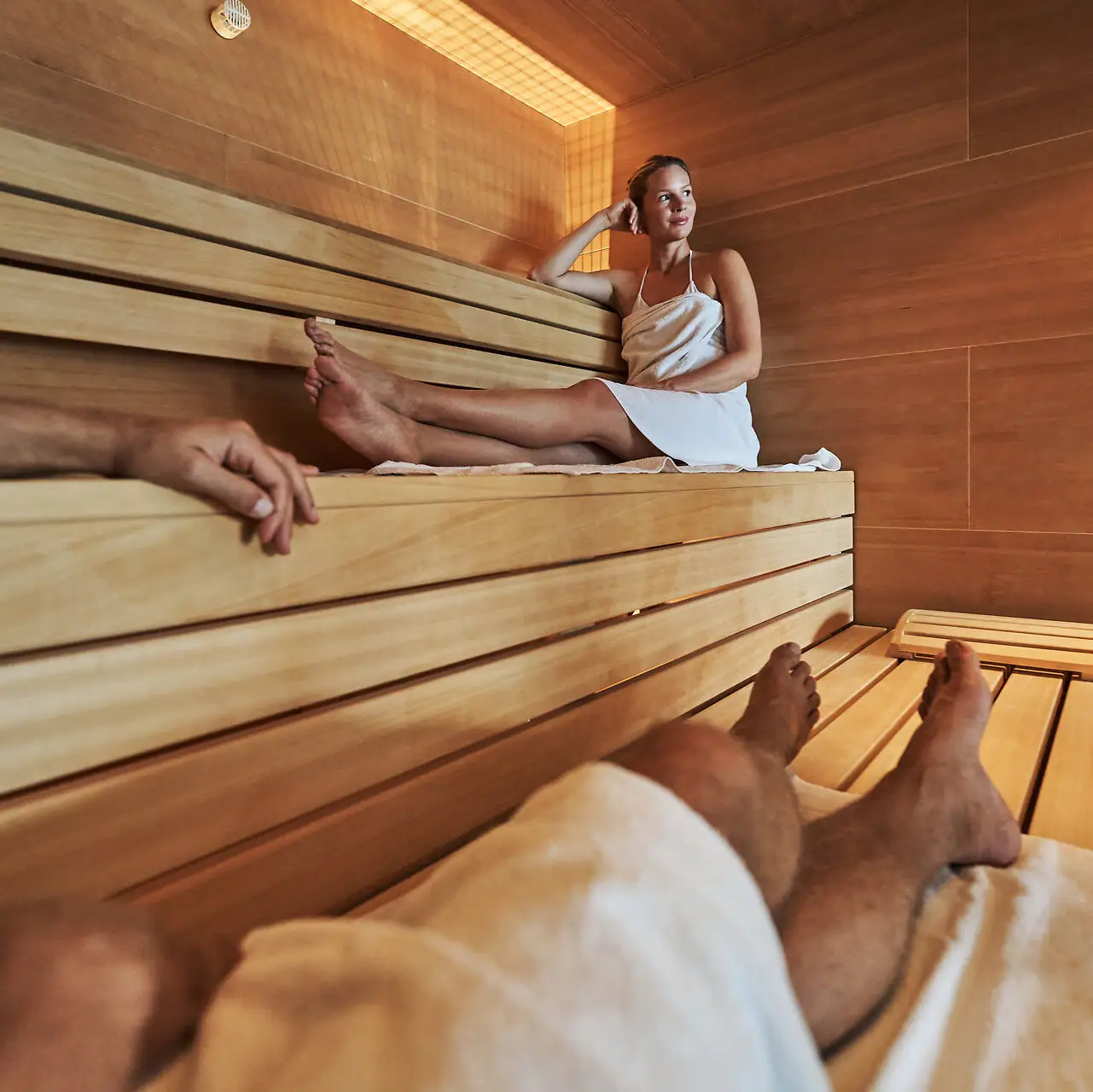 A woman sits on a wooden bench in a sauna.