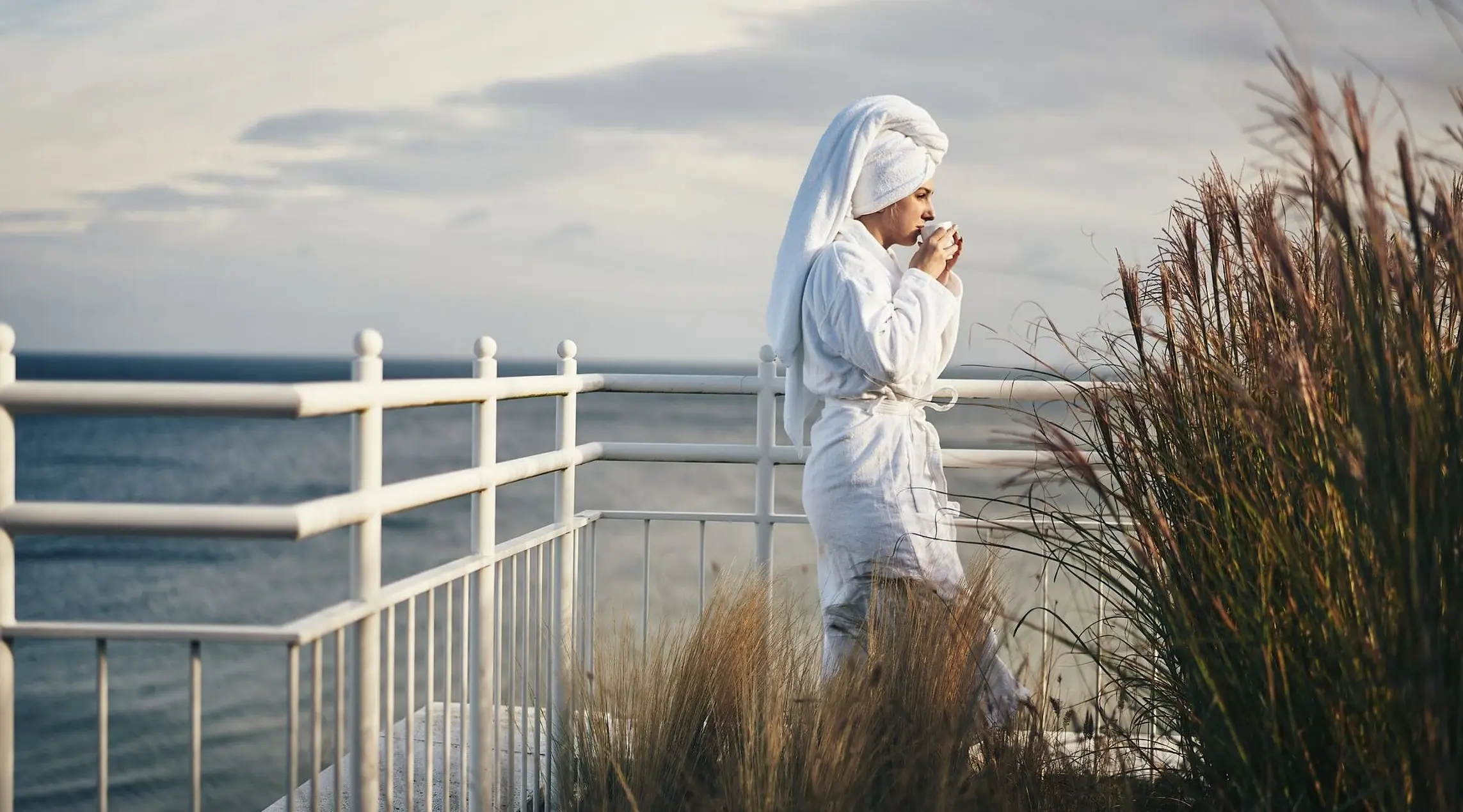 Woman in a bathrobe drinking from a cup outside.