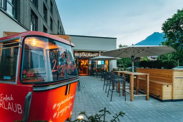 The terrace in front of the aja Garmisch-Partenkirchen with a gondola and some seating and mountains in the background.