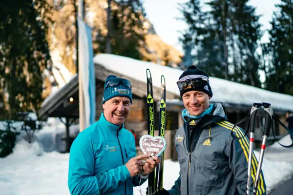 Two men holding skis and smiling.