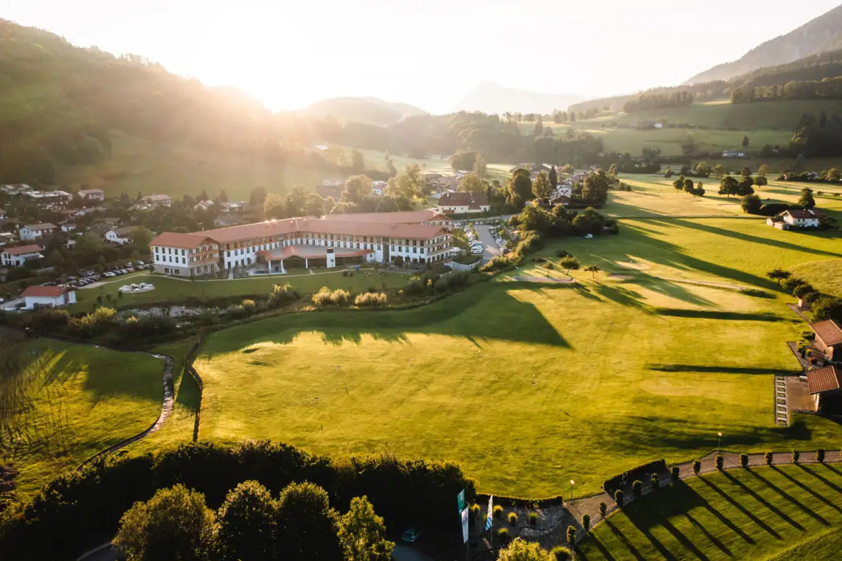 aja Hotel in Ruhpolding A large green field with a large hotel building and trees in the background.