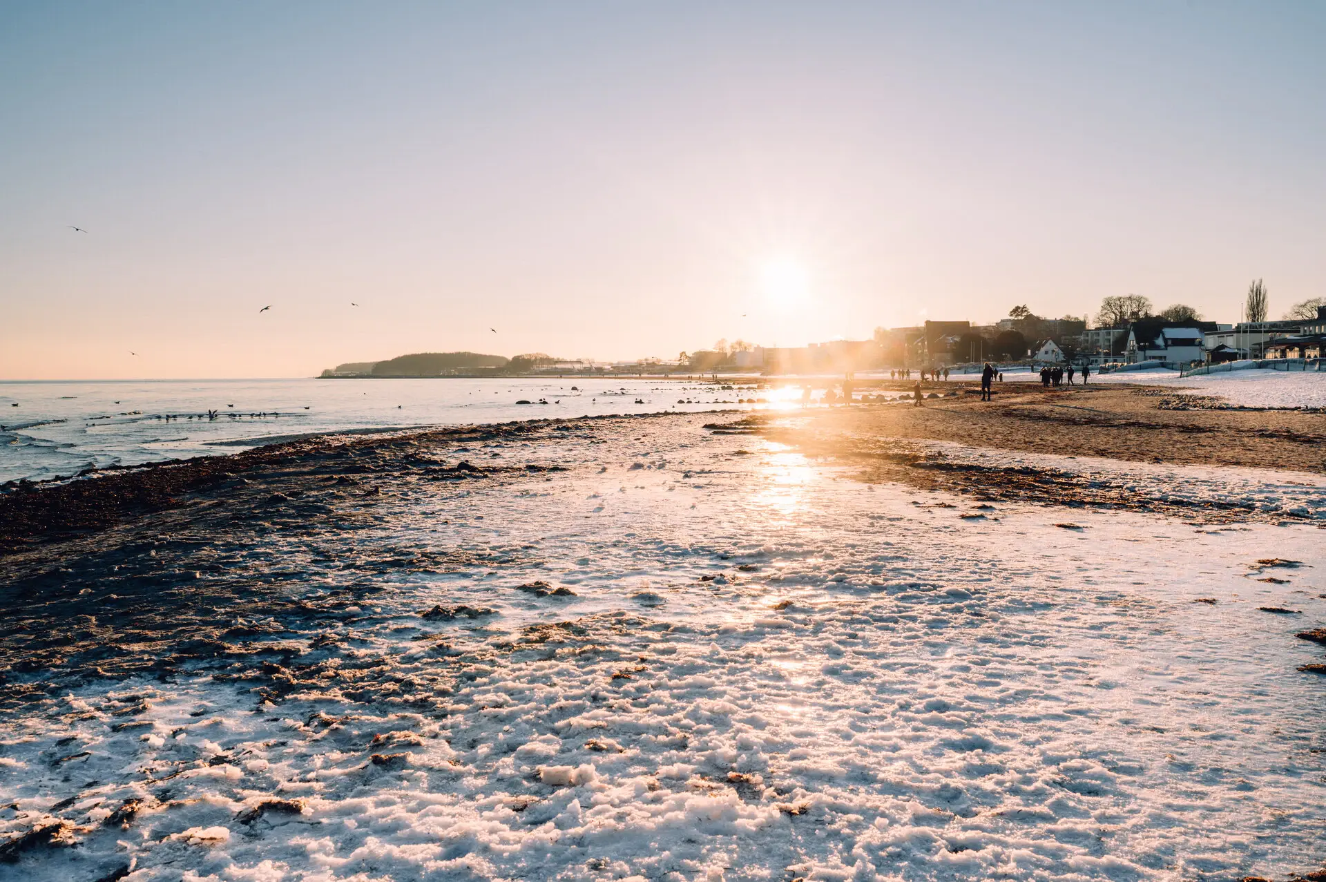 Ein verschneiter Strand mit Wasser und Gebäuden im Hintergrund.