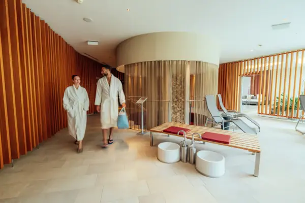 A man and a woman in white bathrobes are walking through a room.