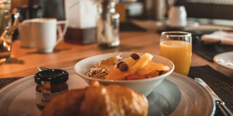 A bowl of muesli and fruit on a plate with a croissant and jam.