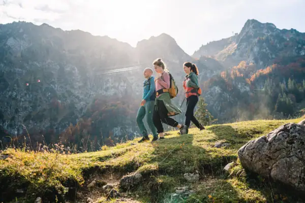 A group of people walking on a hill with mountains in the background.