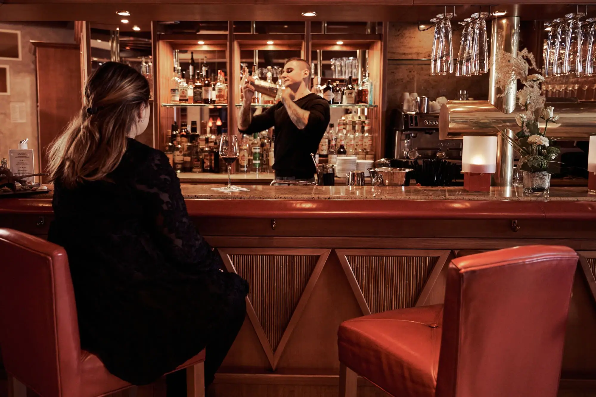 A man in a black dress sits at a bar with a woman in a black dress.