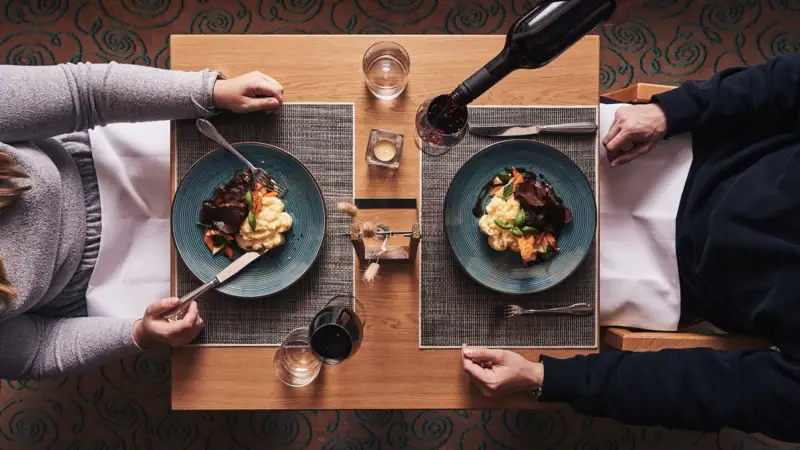 Dinner Nordperd & Villas A person holds a bottle of wine and eats.