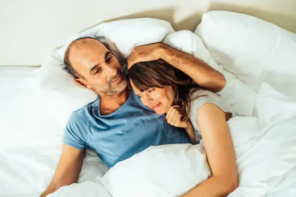 Cuddling in bed A man and a woman are lying in bed.