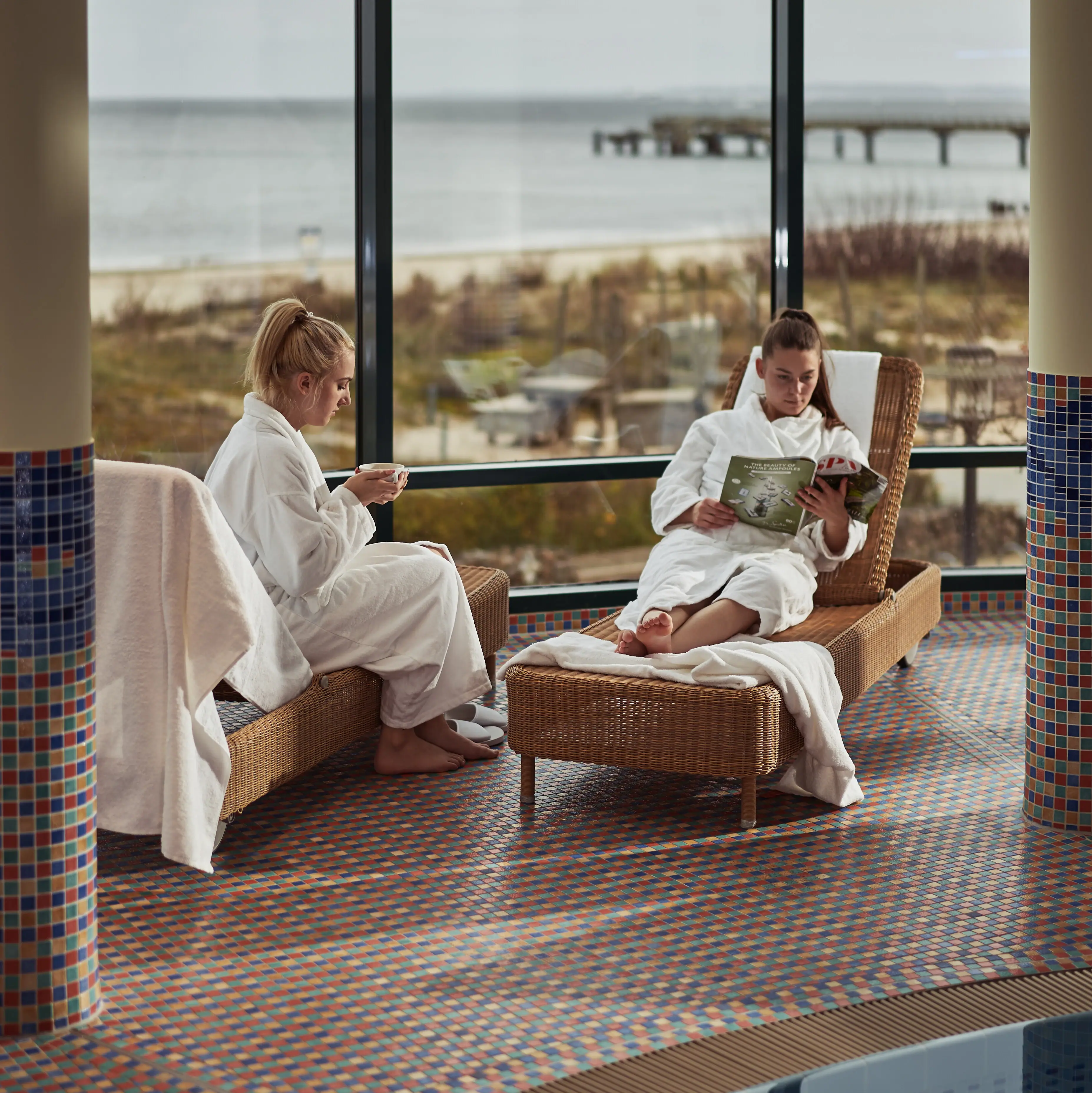 Wellness in Bansin Two women in white bathrobes sit on chairs by the pool.