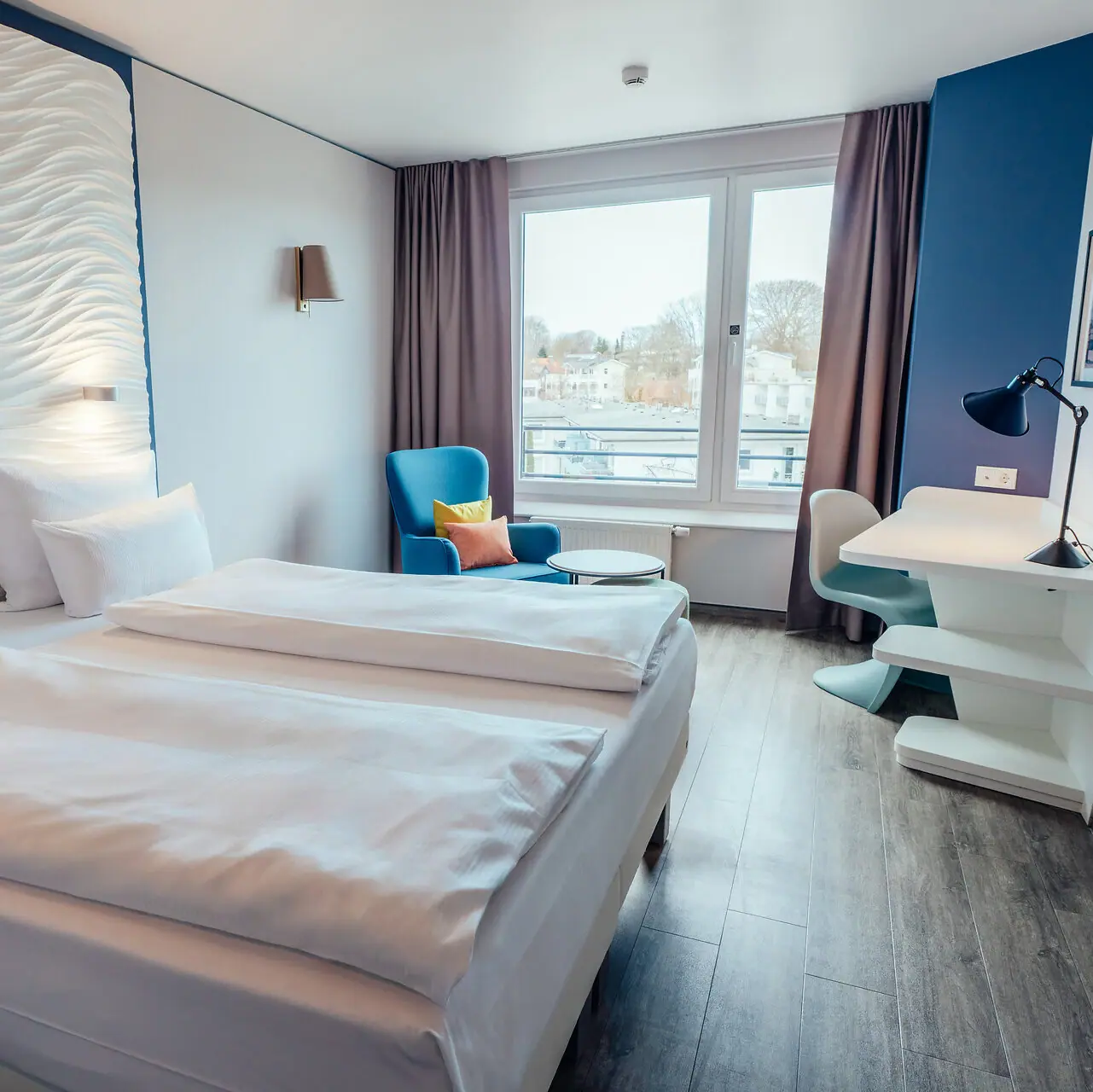 A room with two beds and a table, featuring neatly arranged bedding and pillows.