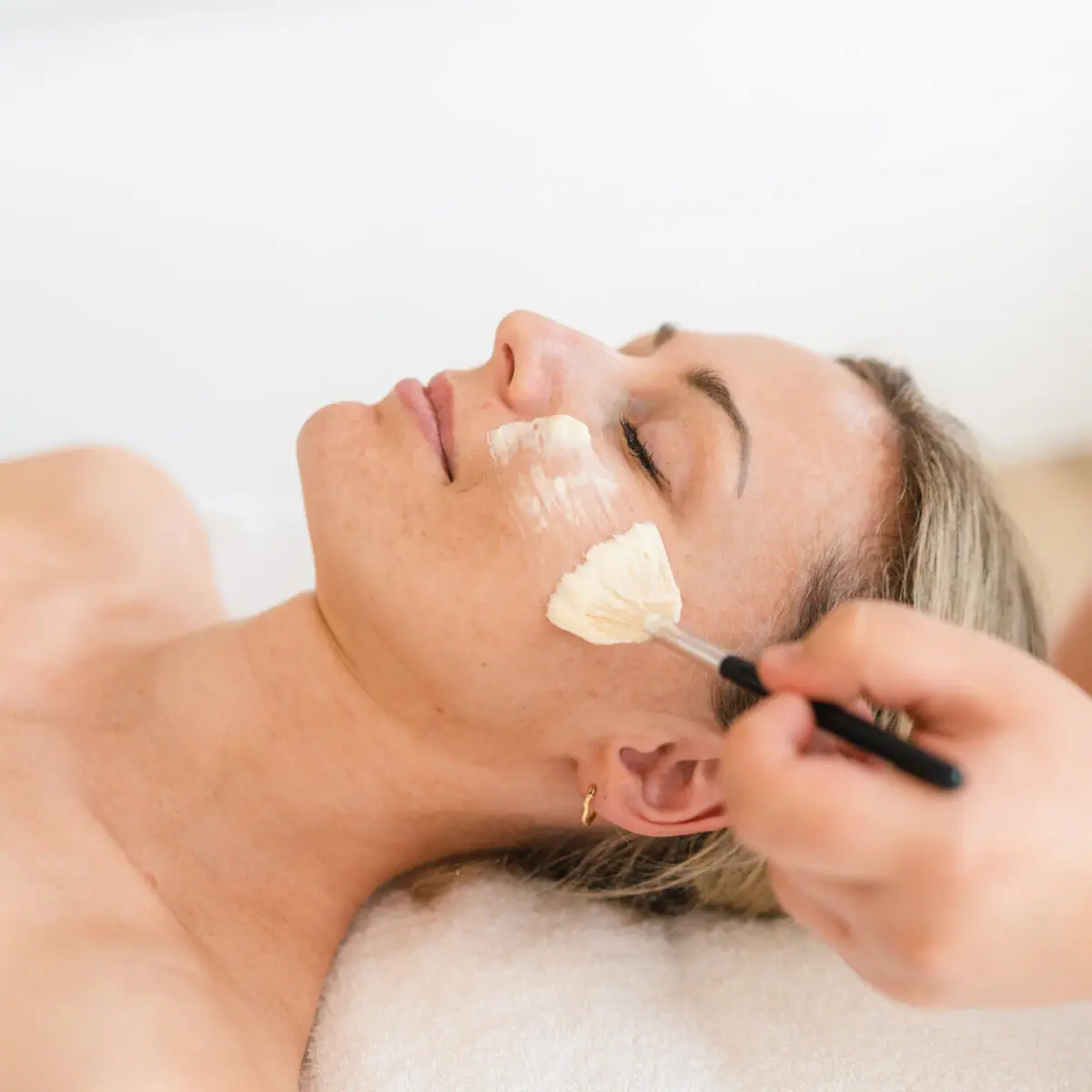 Facial application A woman lies with a paintbrush on her face.