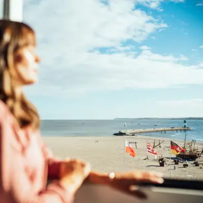 A woman looks out of a window onto a beach.