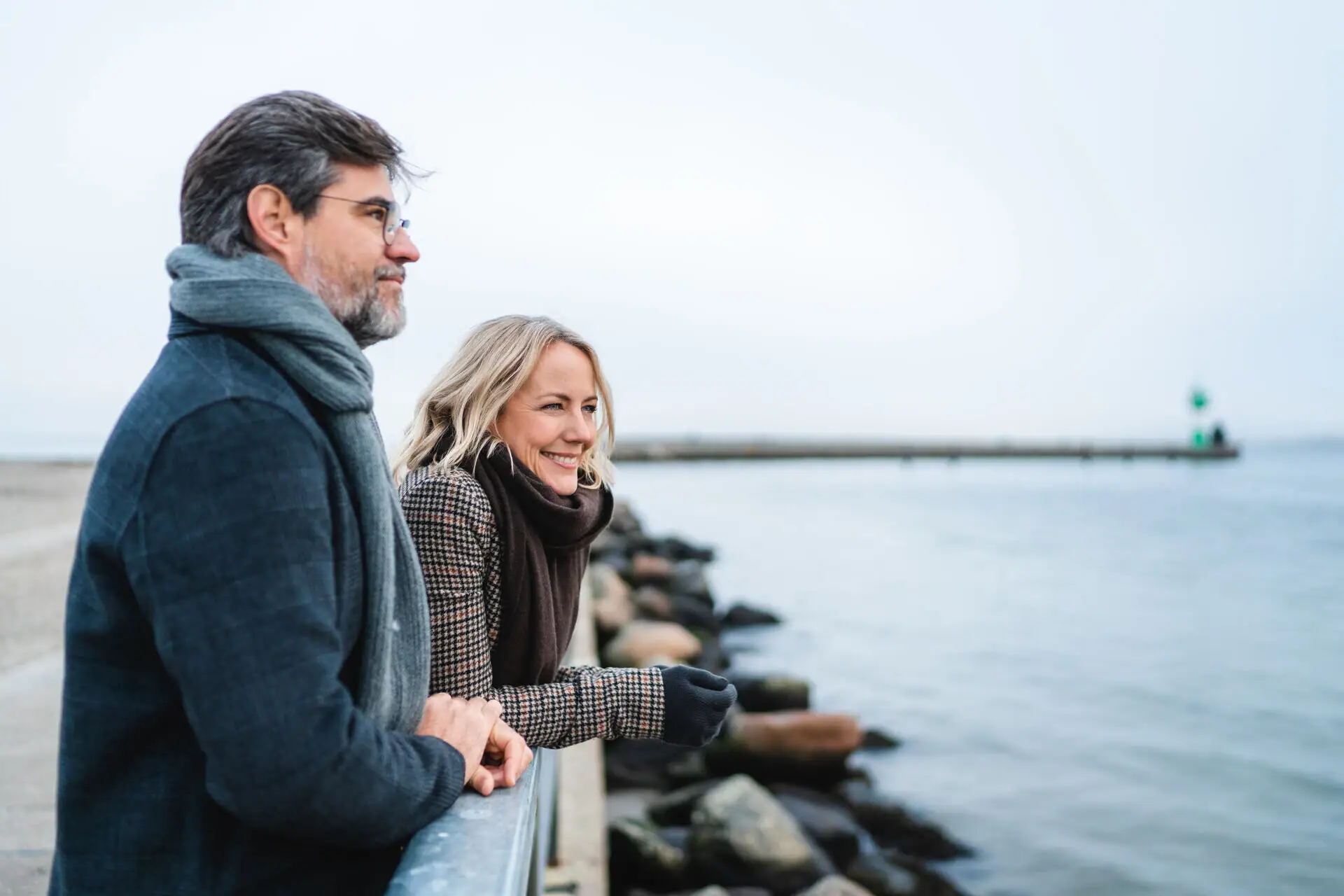 A man and a woman lean against a railing and look out over the water.