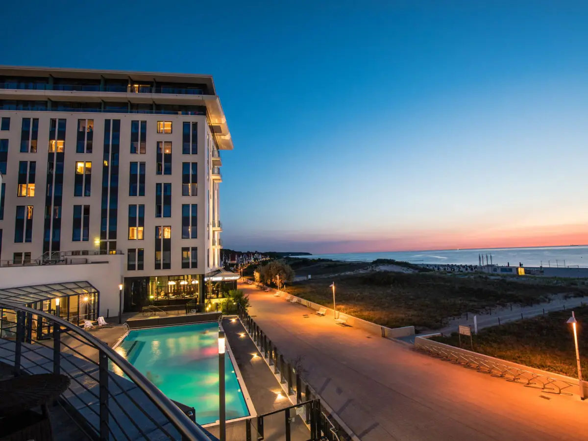 New Year's Eve at aja Warnemünde The hotel building with a pool and a walkway by the sea.