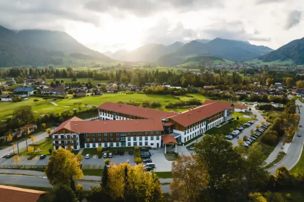aja Ruhpolding A large building with a parking lot in front, surrounded by trees and a cloudy sky.