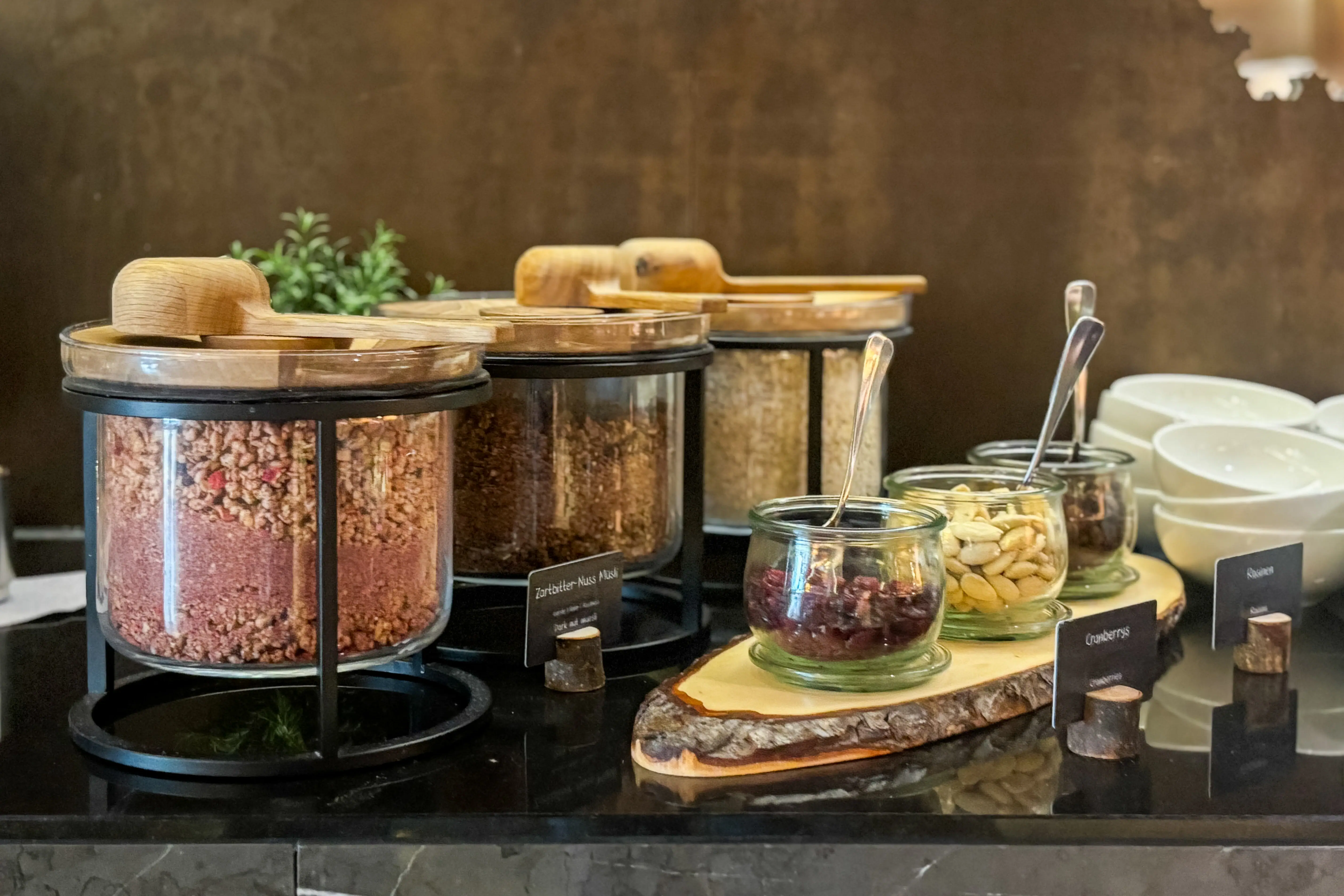 A counter with different types of muesli in containers. Next to it are nuts and seeds.