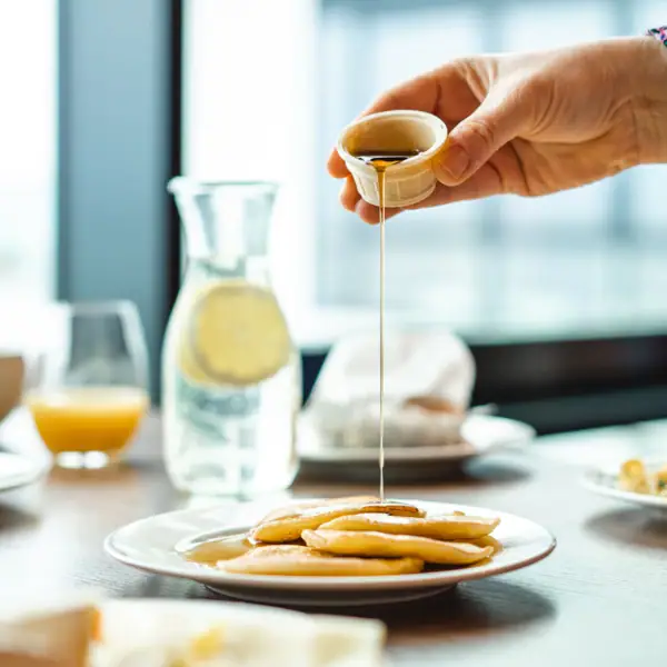 One person pours syrup onto a plate of pancakes.