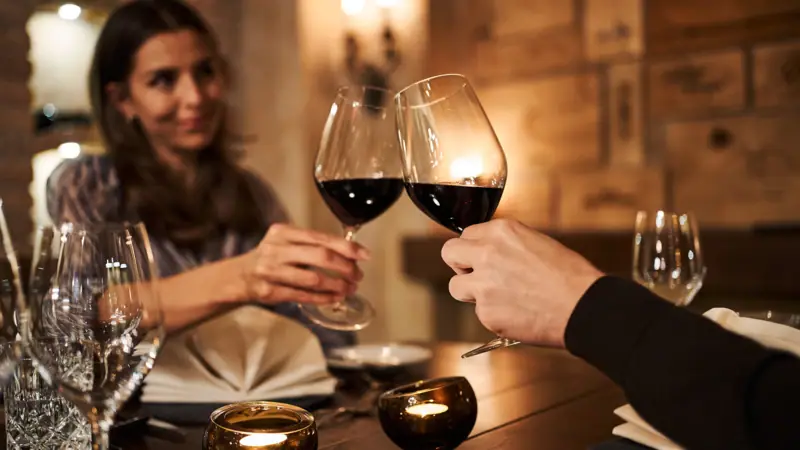 A man and a woman are clinking their wine glasses at a table.