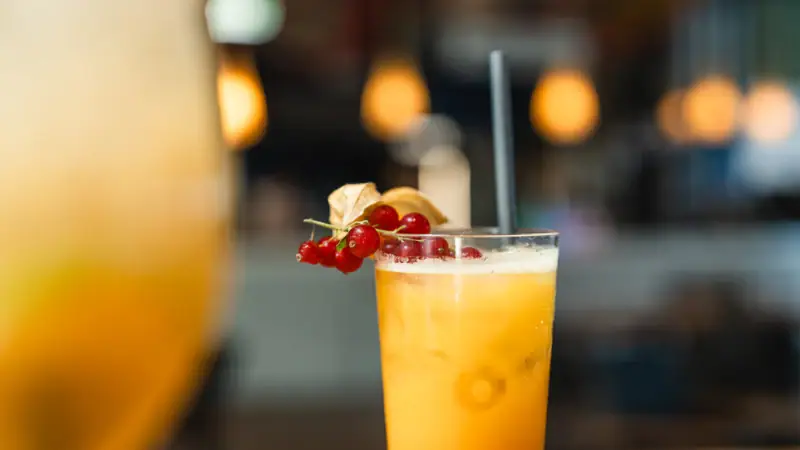 A glass of orange juice with a straw and berries.