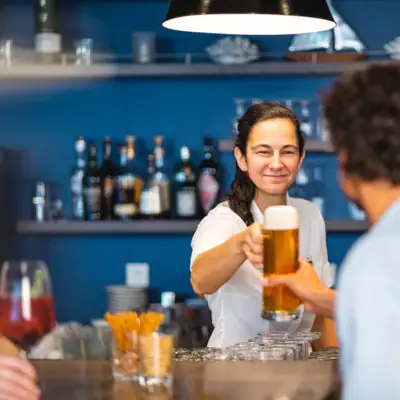 A woman holds a glass of beer and stands at the bar with a guest.