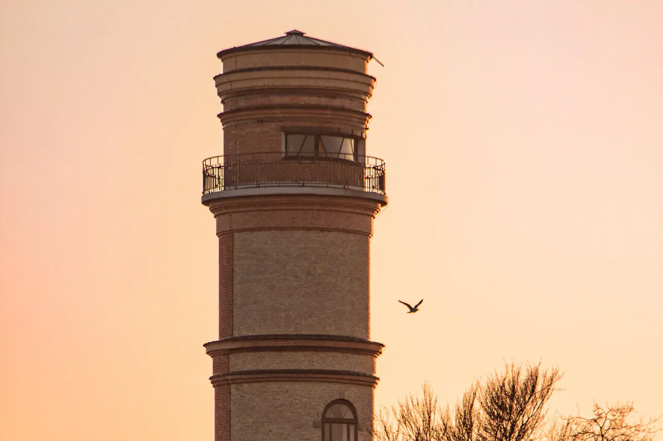 A lighthouse with a bird flying in the sky.